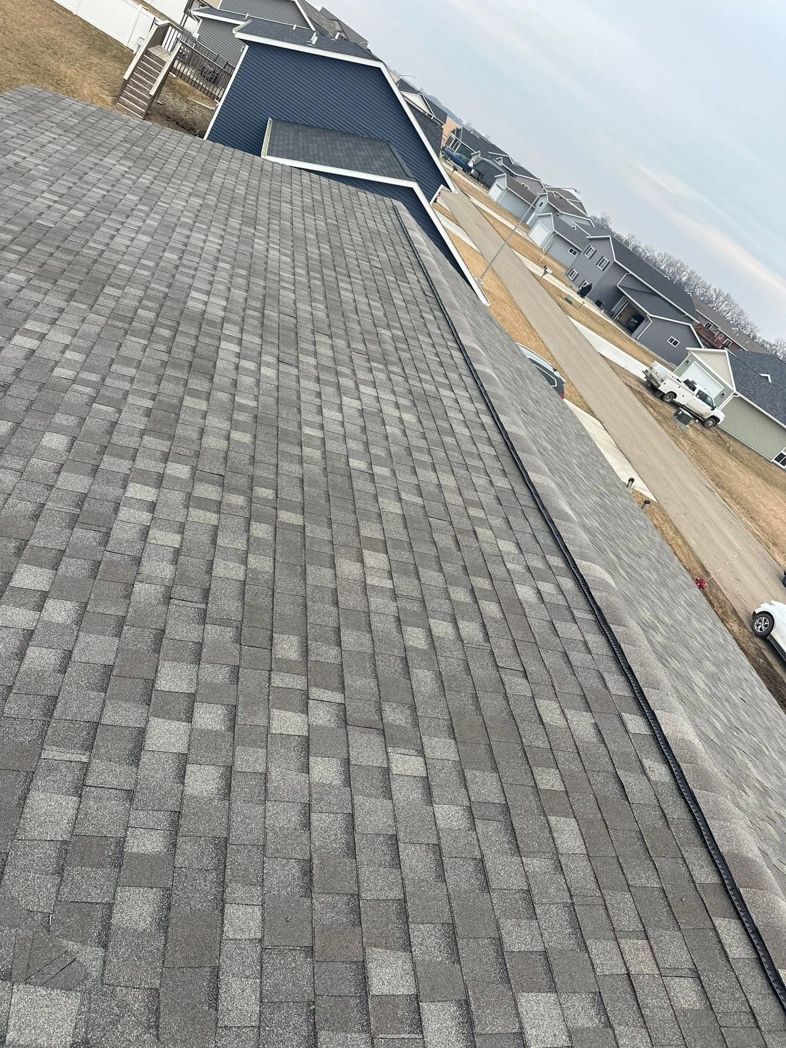 Fresh gray architectural shingles on a roof with new construction in the background