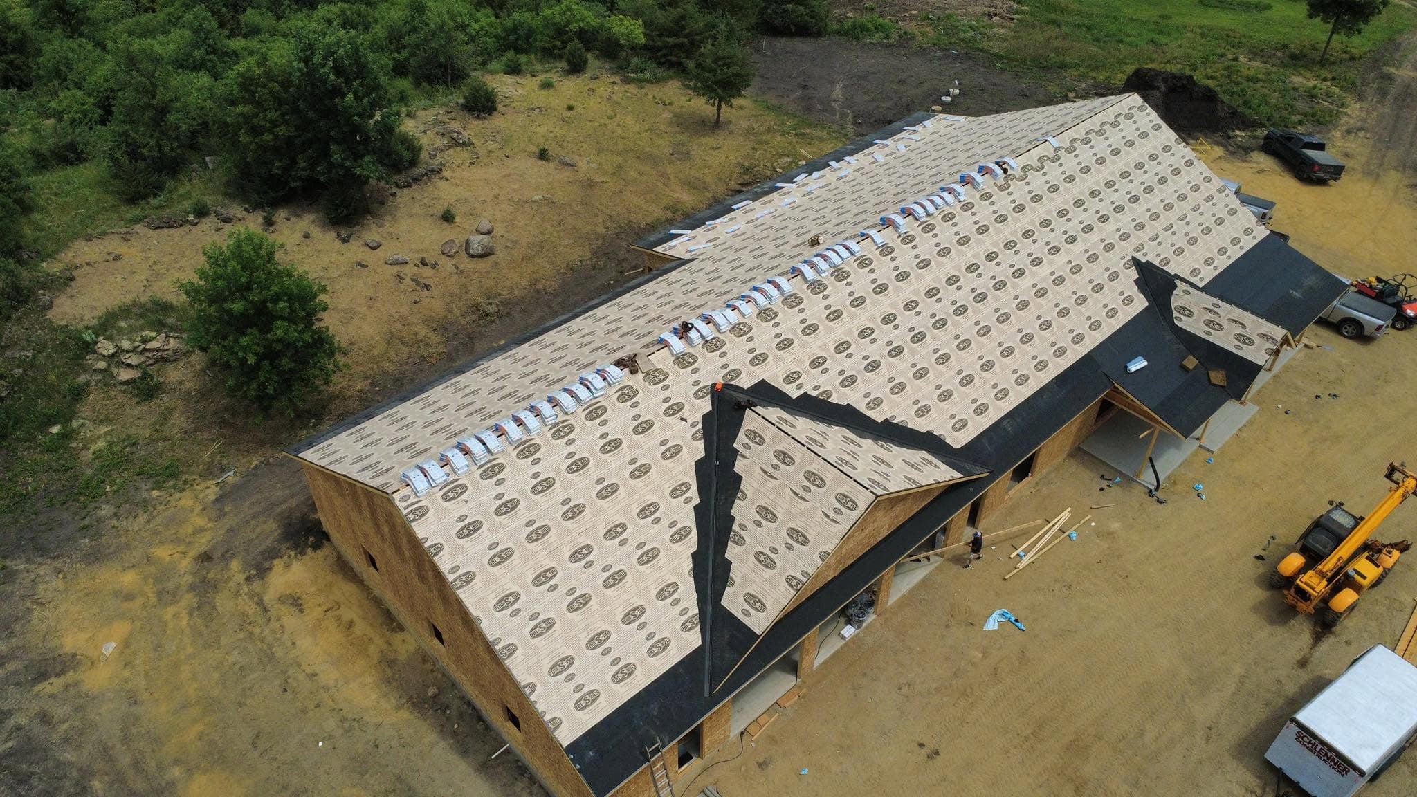 Drone view of a large commercial building mid re-roof with underlayment rows down and a telehandler alongside