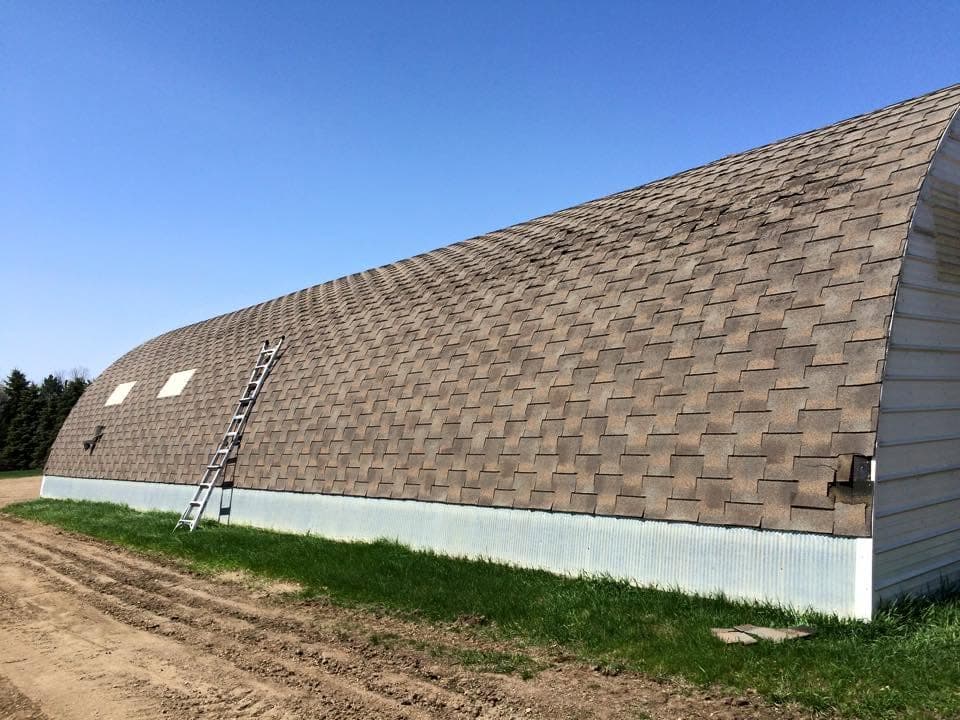 Arched quonset building shingled end to end with a ladder set against the curve
