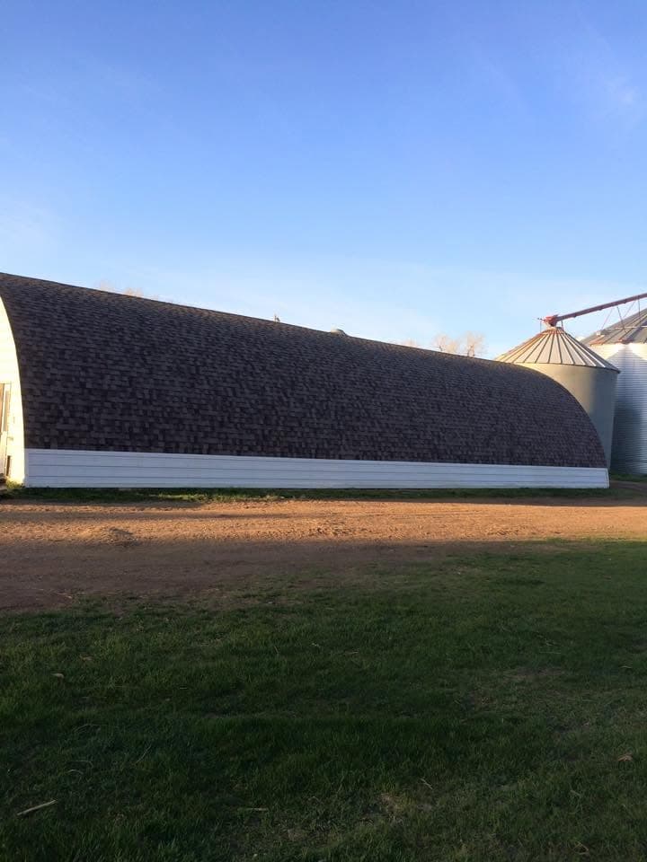 Long shingled quonset building beside grain bins