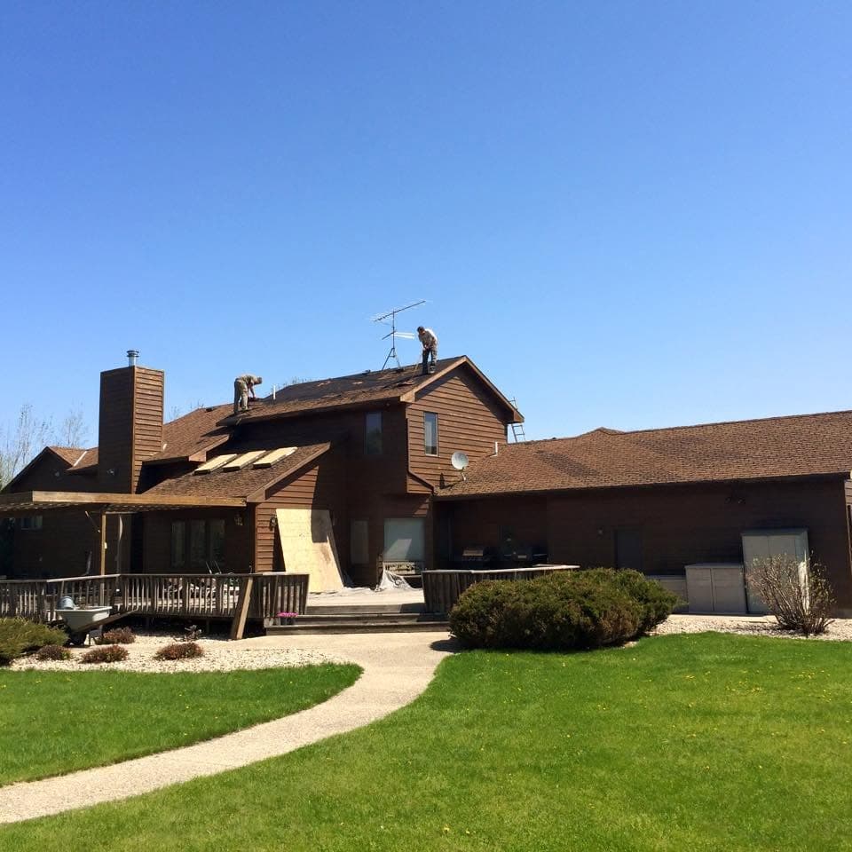 Crew working the roof of a two-story home with a brick chimney under a clear sky
