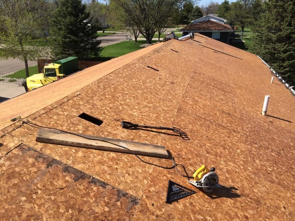 New shingle courses being installed across a roof face with tools staged