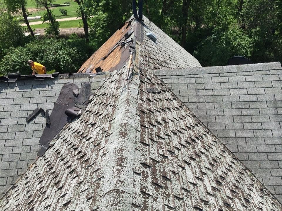 Weathered, wind-worn shingles coming off a steep hip roof with the crew at the peak