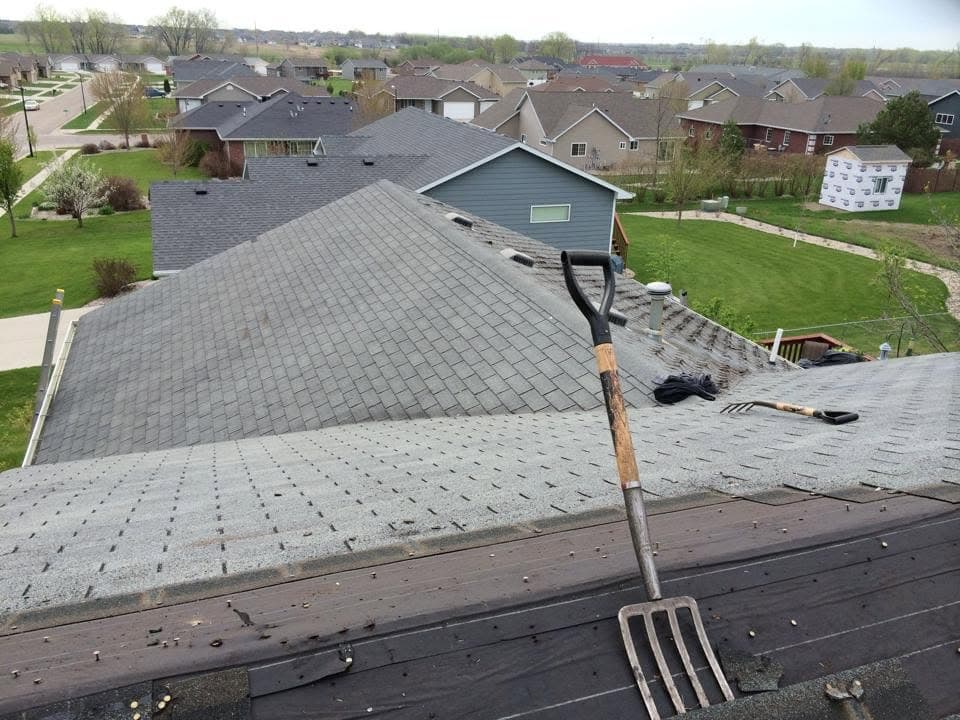 Roof edge mid tear-off with a fork resting against stripped decking