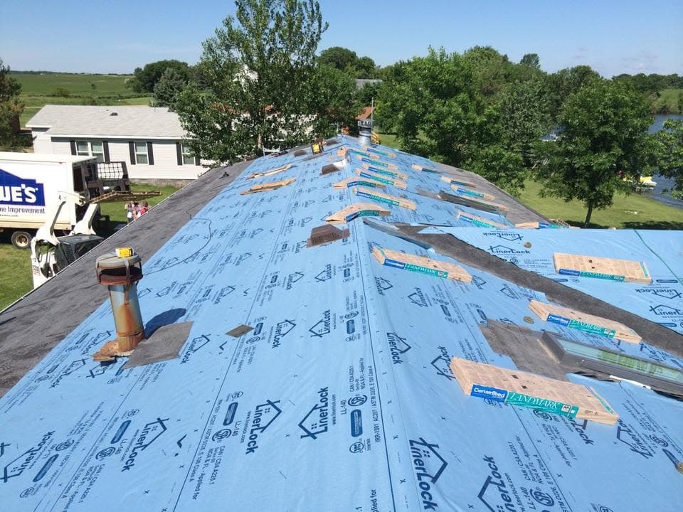 Synthetic underlayment rolled out along a ridge with shingle bundles staged